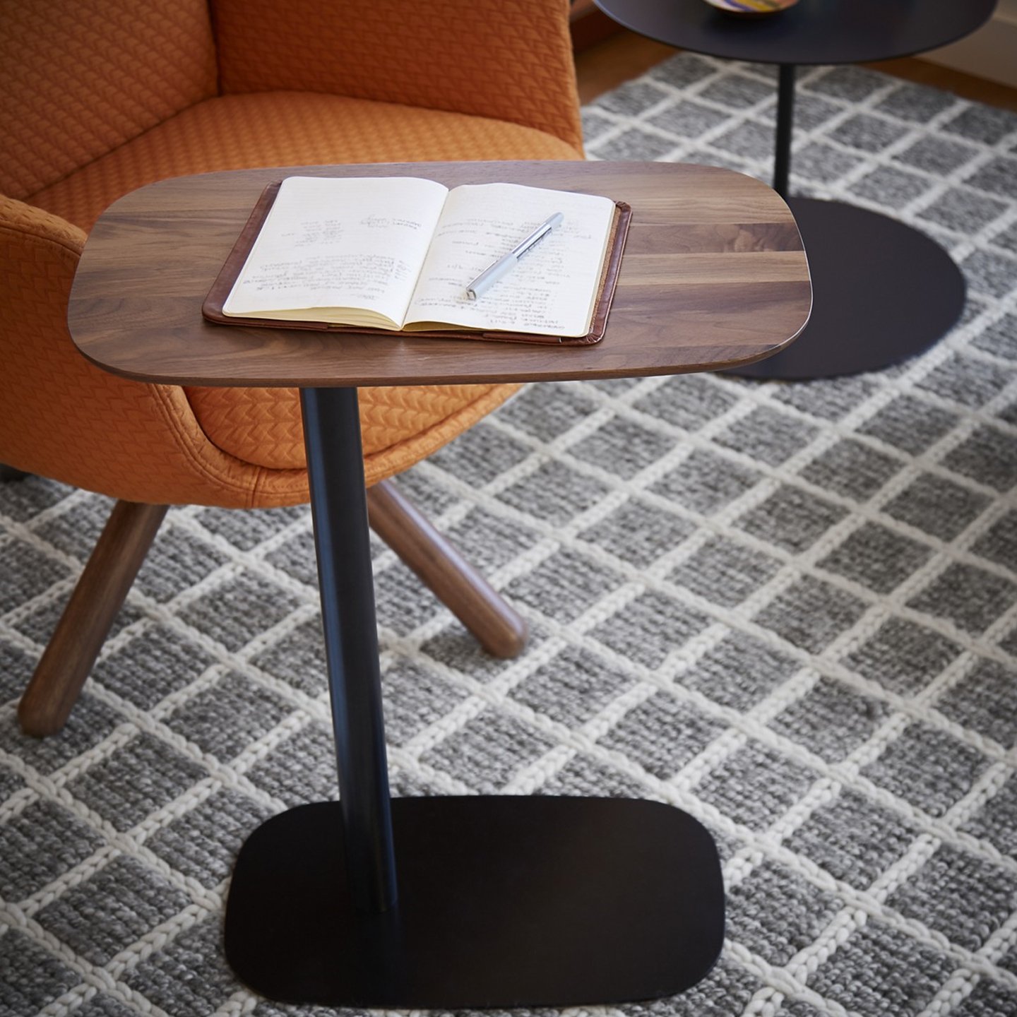 Haworth Pip Laptop table in walnut hardwood and a black steel base next to orange chair and notebook on it