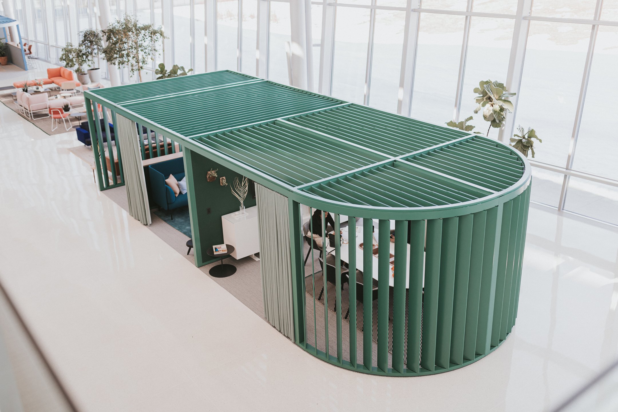 Haworth Pergola Workspace in green color and curtains in open office space with employees working at white desk and white storage space