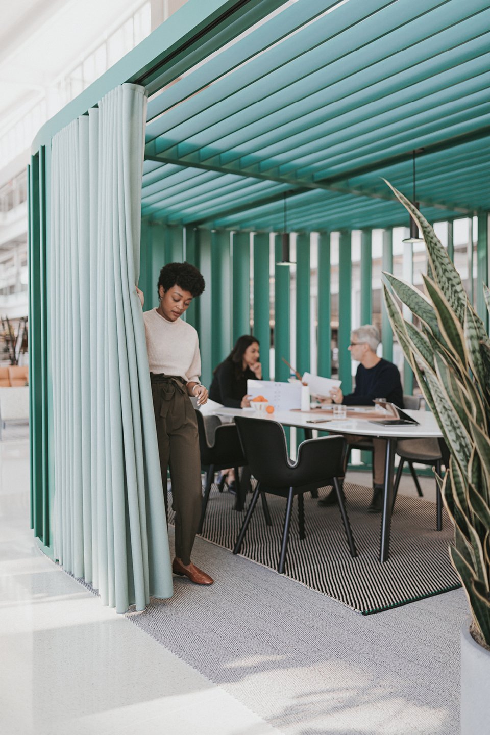 Haworth Pergola Workspace with blue trip and light blue curtain being closed for privacy while employees work at desk in open office space
